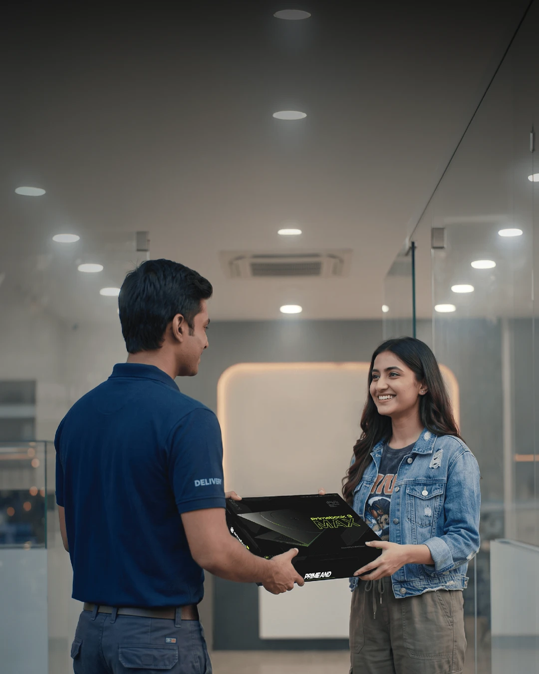 A delivery person handing a boxed Primebook 3 Max laptop to a smiling customer in a store